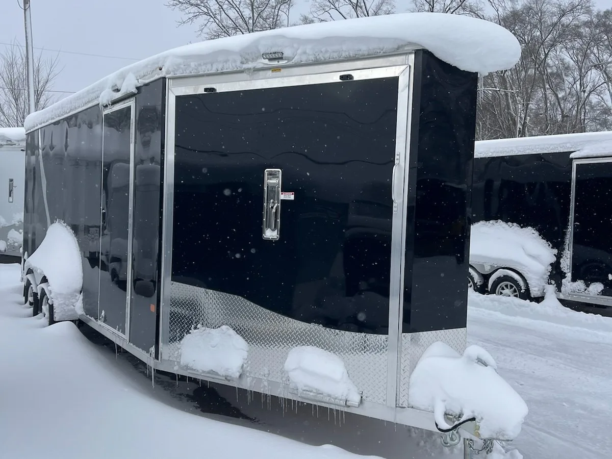 Black enclosed aluminum snowmobile trailer covered in snow